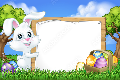 The Easter Bunny Rabbit peeking around a sign background and pointing at it in a park or field with Easter eggs.