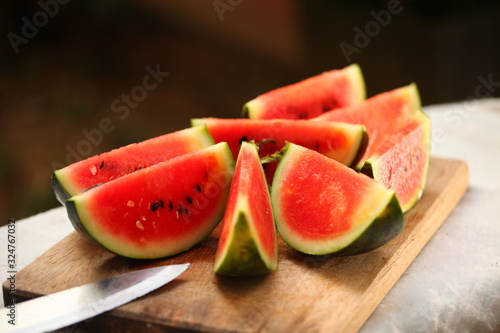 cutting fresh ripe watermelon into pieces with a knife on a wooden table