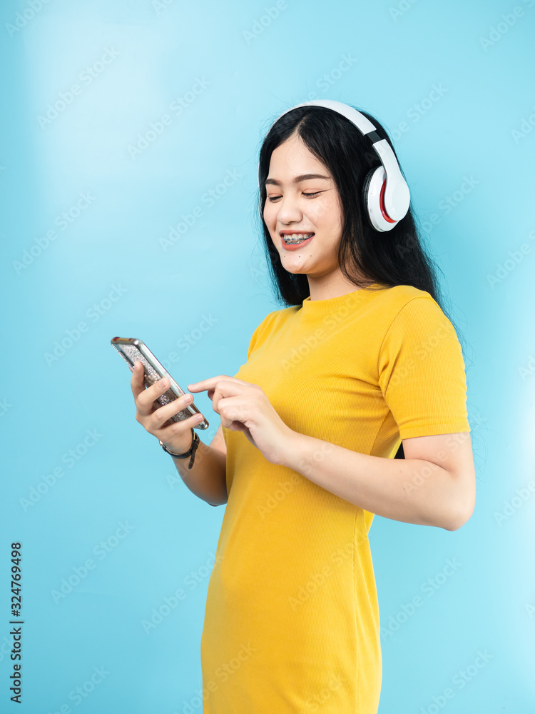 Happy Asian woman using headphone and smartphone on blue background. Happy Asian woman using headphone and smartphone on blue background.