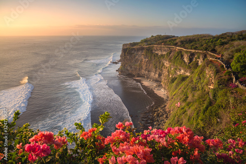 Scenery of Uluwatu cliff with colorful flowers foreground before sunset in Bali, Indonesia.