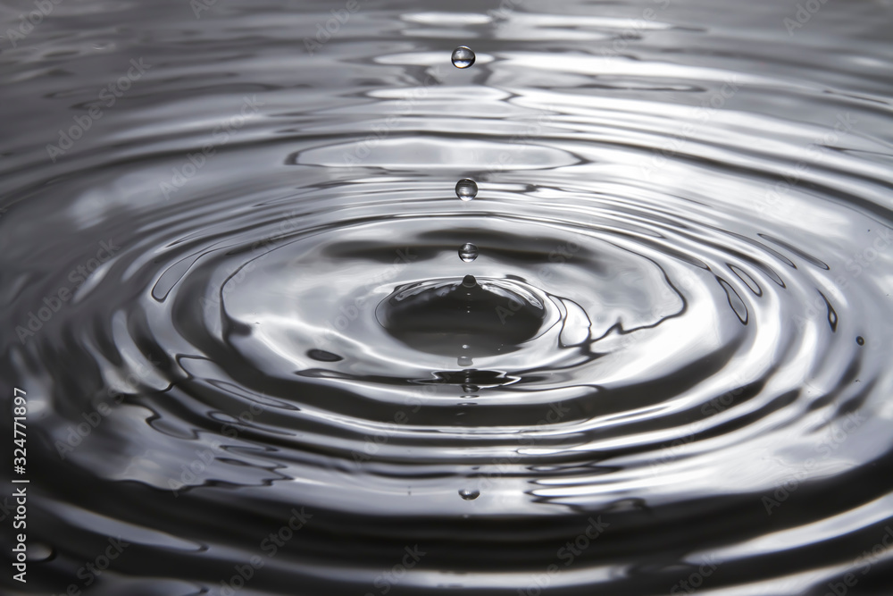 Water droplets falling against the surface of the water create a beautiful ripple on the gray water surface. Water droplets falling against the surface of the water create a beautiful ripple on the gray water surface.