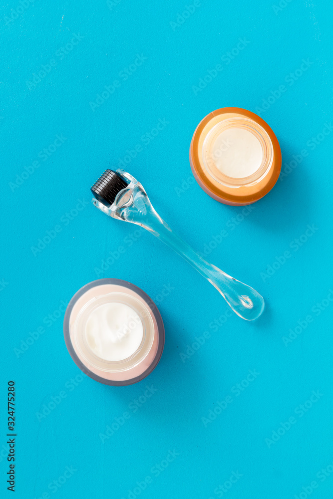Dermaroller for mesotherapy near creams on blue background top-down flat lay Dermaroller for mesotherapy near creams on blue background top-down flat lay