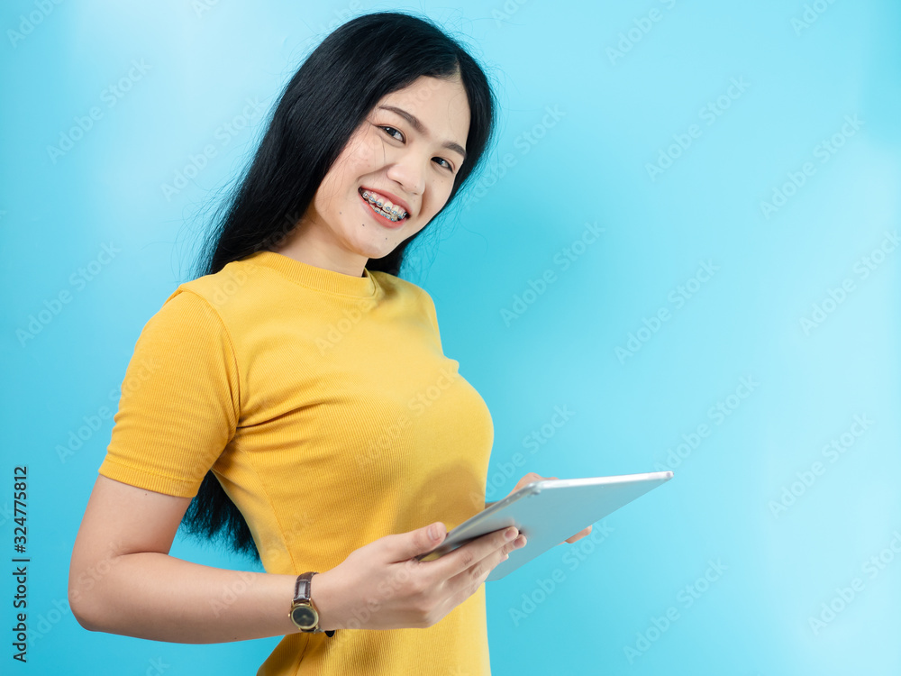 Happy Asian woman in yellow dress using tablet on blue background. Happy Asian woman in yellow dress using tablet on blue background.
