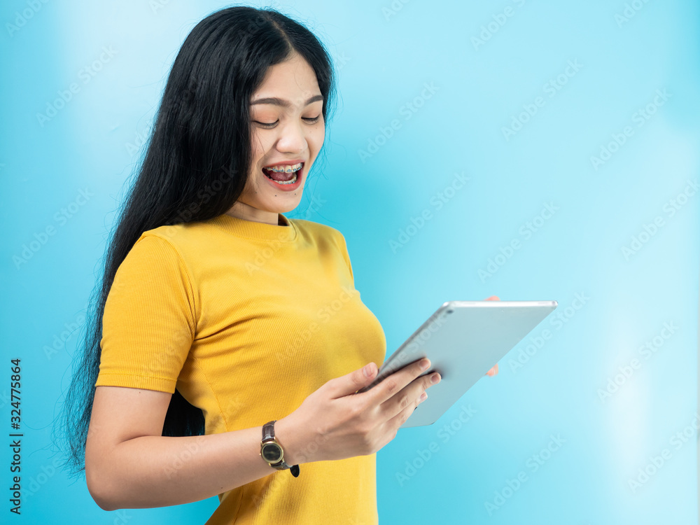 Happy Asian woman in yellow dress using tablet on blue background. Happy Asian woman in yellow dress using tablet on blue background.