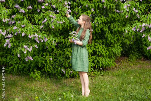 Cute girl has fun in the park with blooming lilacs, enjoys spring and warmth