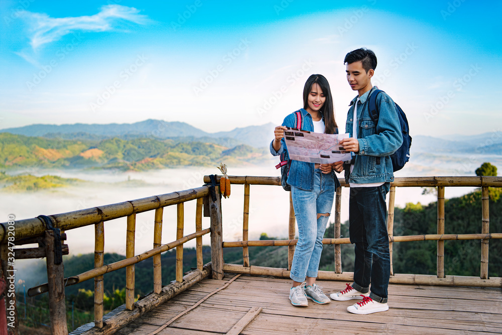 Asian tourist man and woman travel with map in forest. Beautiful Travelers Smiling Couple In Love have a good time in the mountains ,Holding camera In Hands While Traveling Together. Travel Concept
