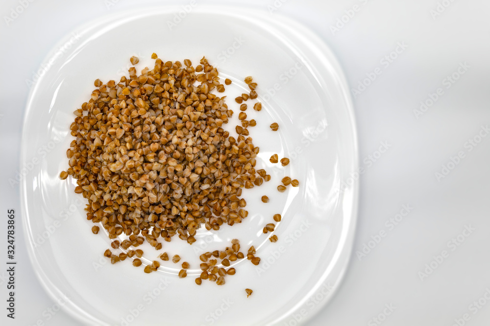 On a white background, a white plate contains buckwheat, seasoned with linseed oil On a white background, a white plate contains buckwheat, seasoned with linseed oil
