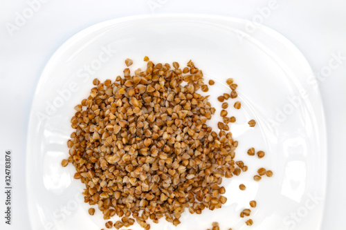 Buckwheat in a small amount lies on a white clean plate, top view