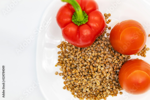 Whole Bulgarian red pepper, two juicy fresh tomatoes and buckwheat in a white plate