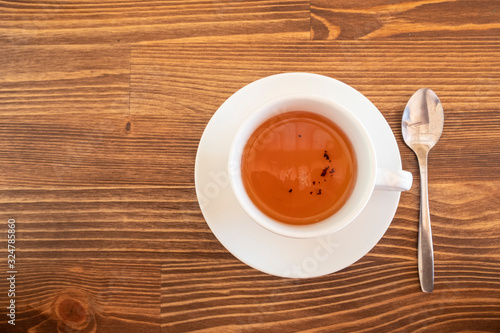 A white cup of tea with teaspoon on a brown wooden table background.