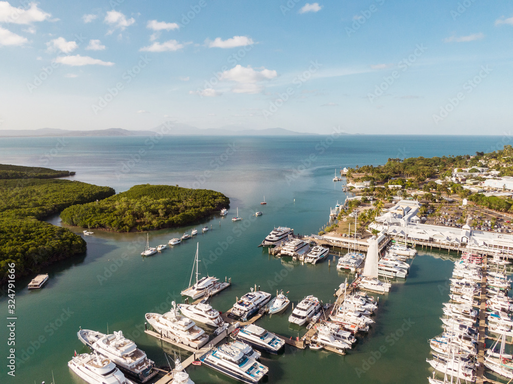 Marina town with waterfront river view of yachts and boats in sea water. Carins Port Douglas aerial view. Dramatic DRONE view from above. Mountain landscape in background. Queenstown, Australia.