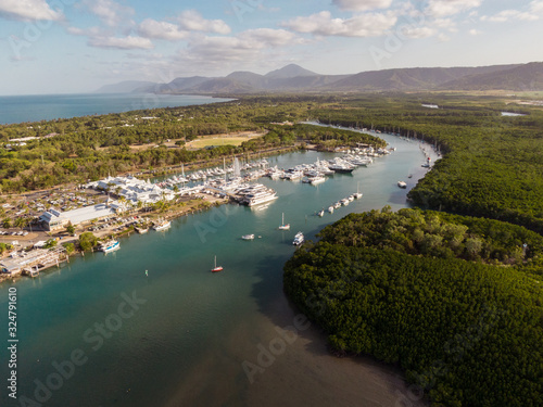 Marina town with waterfront river view of yachts and boats in sea water. Carins Port Douglas aerial view. Dramatic DRONE view from above. Mountain landscape in background. Queenstown, Australia.