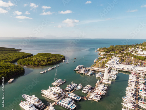 Marina town with waterfront river view of yachts and boats in sea water. Carins Port Douglas aerial view. Dramatic DRONE view from above. Mountain landscape in background. Queenstown, Australia.