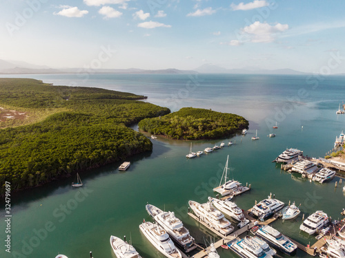 Marina town with waterfront river view of yachts and boats in sea water. Carins Port Douglas aerial view. Dramatic DRONE view from above. Mountain landscape in background. Queenstown, Australia.
