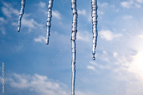 Dangerous icicles on blue sky background. Ice texture. Winter backdrop. Ice texture.
