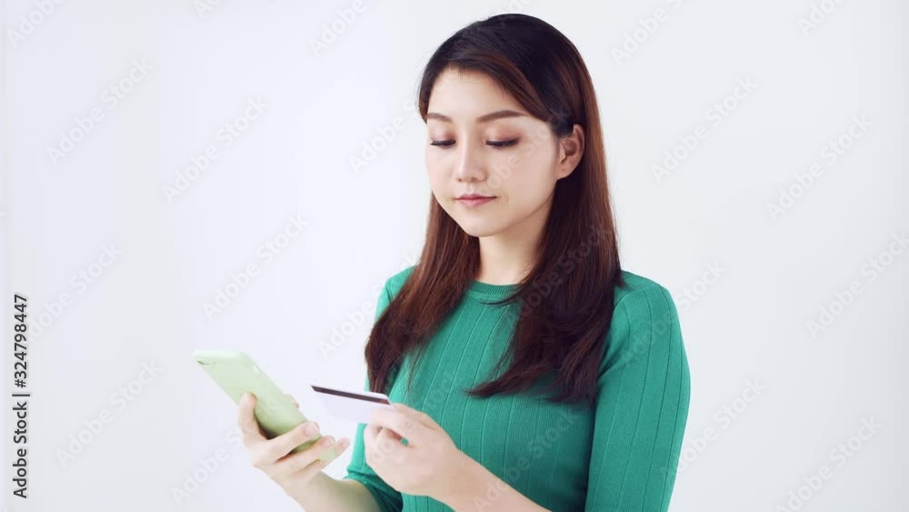 Smiling asian woman shopping via smartphone and paying for her purchase with credit card isolated Smiling asian woman shopping via smartphone and paying for her purchase with credit card isolated