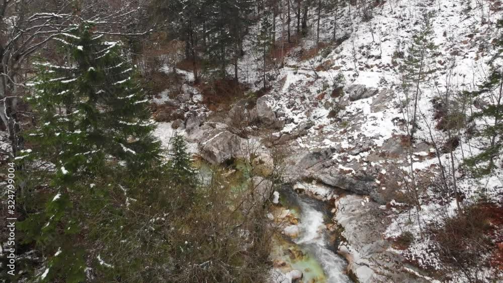 Drone flies over river canyon in winter, trees and slopes covered in snow, crystal clear mountain stream peacefully flowing through riverbeds in morning. Drone flies over river canyon in winter, trees and slopes covered in snow, crystal clear mountain stream peacefully flowing through riverbeds in morning.