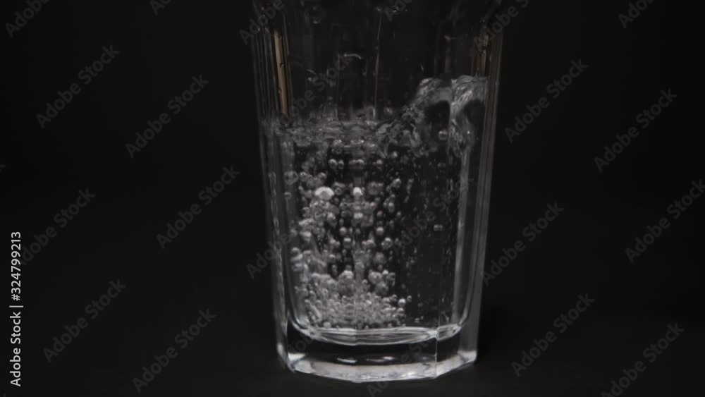 a stream of water is pouring into a large glass, on a black background, with bubbles, slowly, slow mo, large frame a stream of water is pouring into a large glass, on a black background, with bubbles, slowly, slow mo, large frame