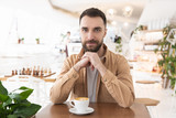 young bearded attractive man drinks coffee during his lunch break in the cafe, positive vibes