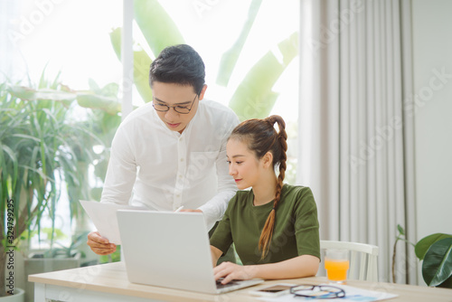 Wide shot of smiling couple surfing in laptop sitting at table © makistock