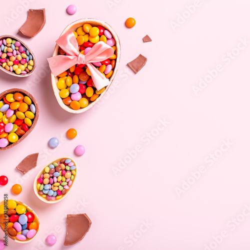 Easter border with chocolate eggs and colorful candy sweets on pastel pink, copy space. Traditional Easter treats flat lay, holiday background
