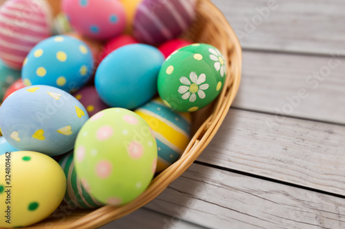 easter, holidays and tradition concept - close up of colored eggs in wicker basket on grey wooden boards background