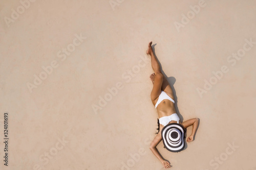 Aerial view of young woman in white  bikini and hat on beach sand in summer concept