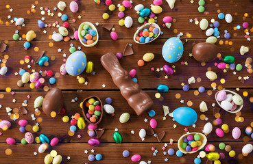 easter, sweets and confectionery concept - chocolate eggs, bunny and candy drops on wooden background