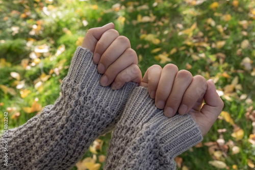 Woman's hands in sweater or pullover on yellow leaves background. Autumn wear.