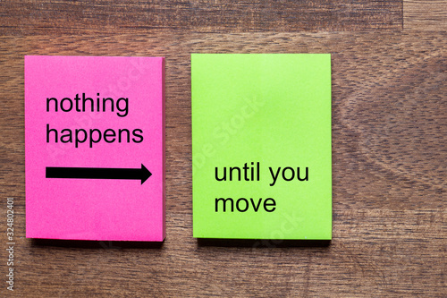 pink and yellow self-adhesive note sticker with the motto: nothing happens until you move. Background dark wooden table