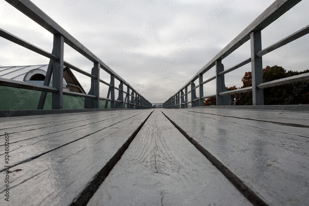 Wooden pedestrian bridge in perspective over roof of Peter and Paul fortress with cloudy sky background.
