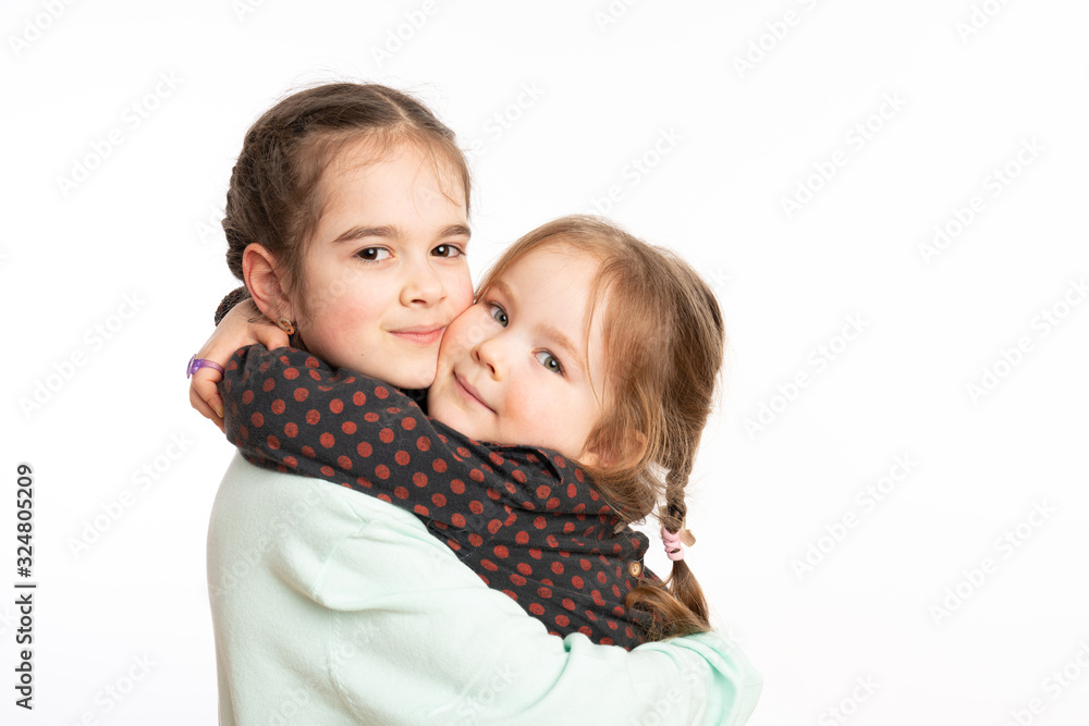 Waist up portrait of two little sisters hugging and looking at the camera isolated over white background with copyspace Waist up portrait of two little sisters hugging and looking at the camera isolated over white background with copyspace