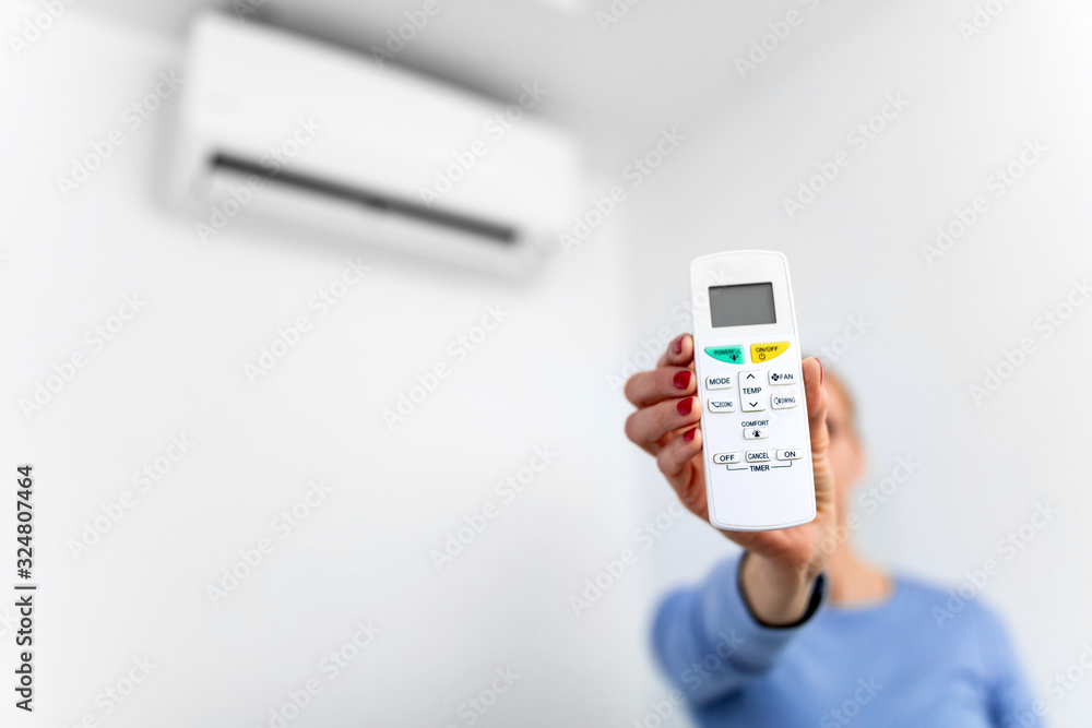 Woman holding a remote of a modern airconditioner unit at home. Woman holding a remote of a modern airconditioner unit at home.