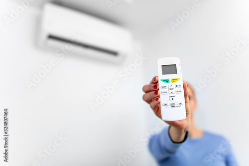 Woman holding a remote of a modern airconditioner unit at home.