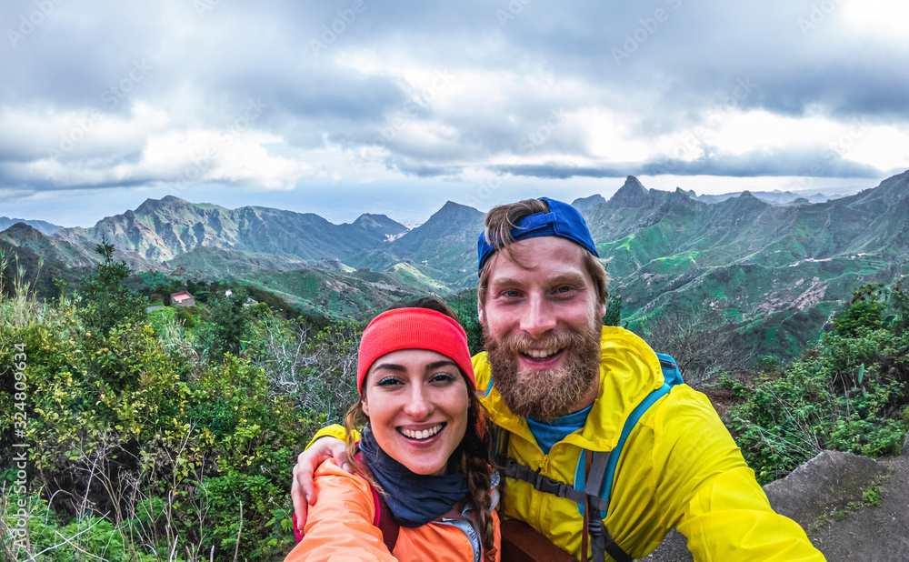 Young hiker couple taking selfie photo at peak of the mountain - Happy millennial people having fun in tour excursion - Travel, adventure and relationship concept - Focus on faces