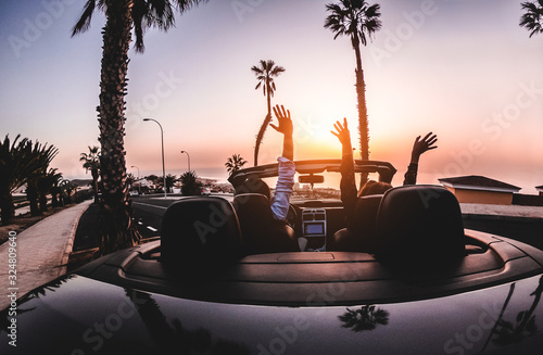 Happy people having fun in convertible car in summer vacation at sunset - Young couple enjoyng holiday on cabriolet auto outdoor - Travel, youth lifestyle and wanderlust concept - Focus on hands