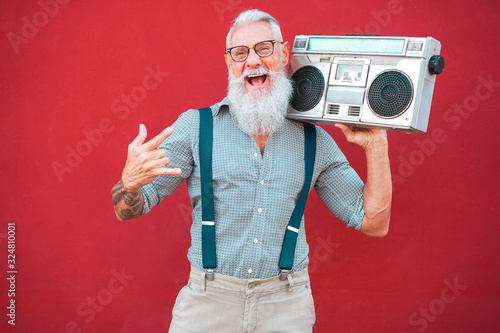 Senior crazy man with 80's boombox stereo playing rock music with red background - Trendy mature guy having fun dancing with vintage radio - Joyful elderly lifestyle concept - Focus on his face photo
