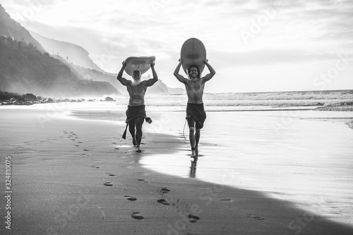 Multigeneration friends going to surf on tropical beach - Family people having fun doing extreme sport - Main focus on young man face - Black and white editing