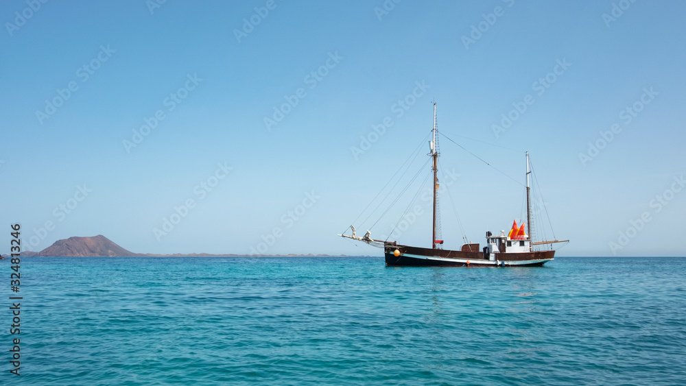 panoramic views of the islet of Los Lobos and a stationary vintage sailing ship or a schooner, operating as day trips and excursions, at Corralejo, Fuerteventura, Canary Islands, Spain
