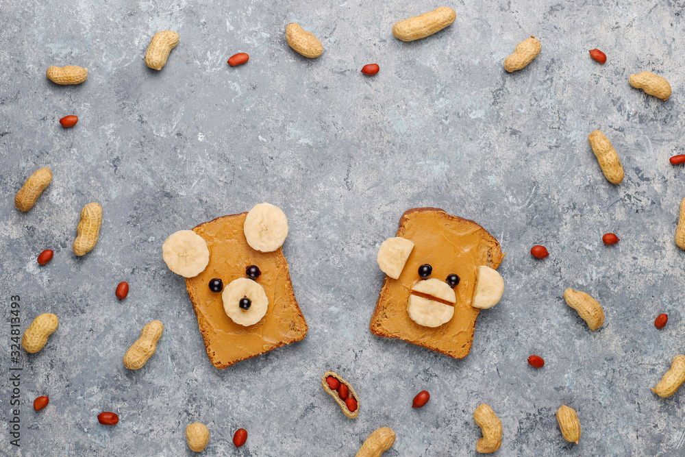Funny bear and monkey face sandwich with peanut butter, banana and black currant,peanuts on grey concrete background,top view Funny bear and monkey face sandwich with peanut butter, banana and black currant,peanuts on grey concrete background,top view