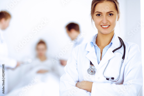 Female doctor smiling on the background with patient in the bed and two doctors