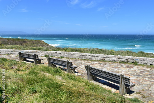 Wooden benches on a beach promenade with turquoise sea, waves and blue sky. Viveiro, Lugo, Galicia, Spain.