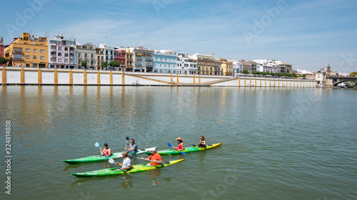 Views of Guadalquivir River with several tourists enjoying canoeing downstream, popular water sport attraction and with Triana neighborhood in the background, Seville, Andalusia, Spain photo