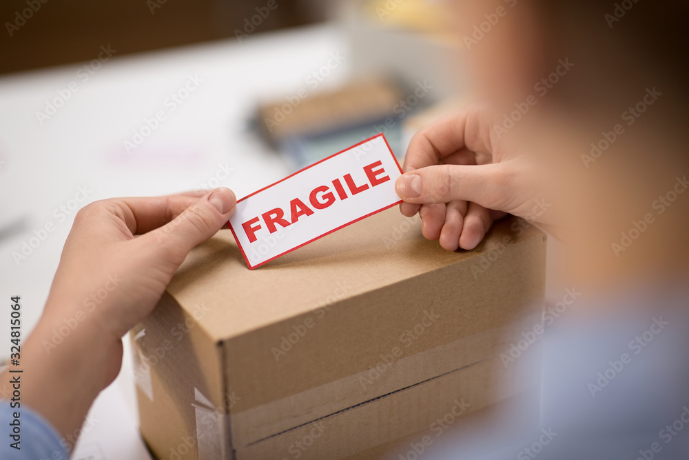 delivery, mail service, people and shipment concept - close up of woman sticking fragile mark to parcel box at post office - obrazy, fototapety, plakaty 