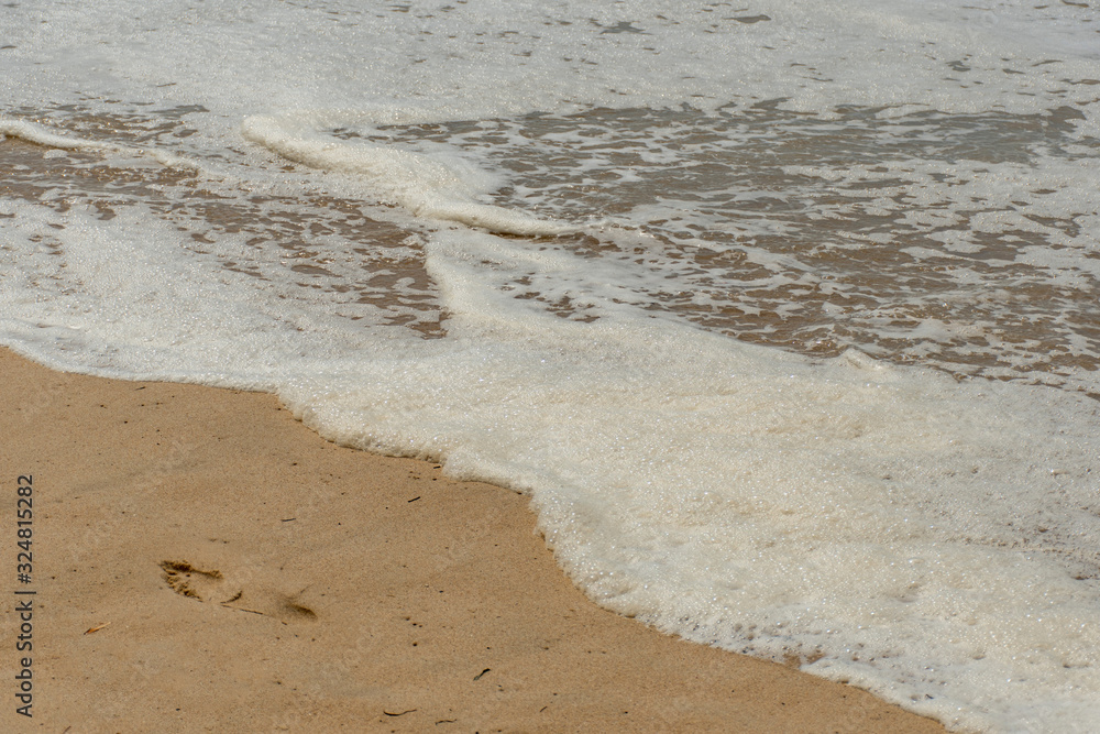Foam in the waves and lonely footprint on a sandy beach Foam in the waves and lonely footprint on a sandy beach