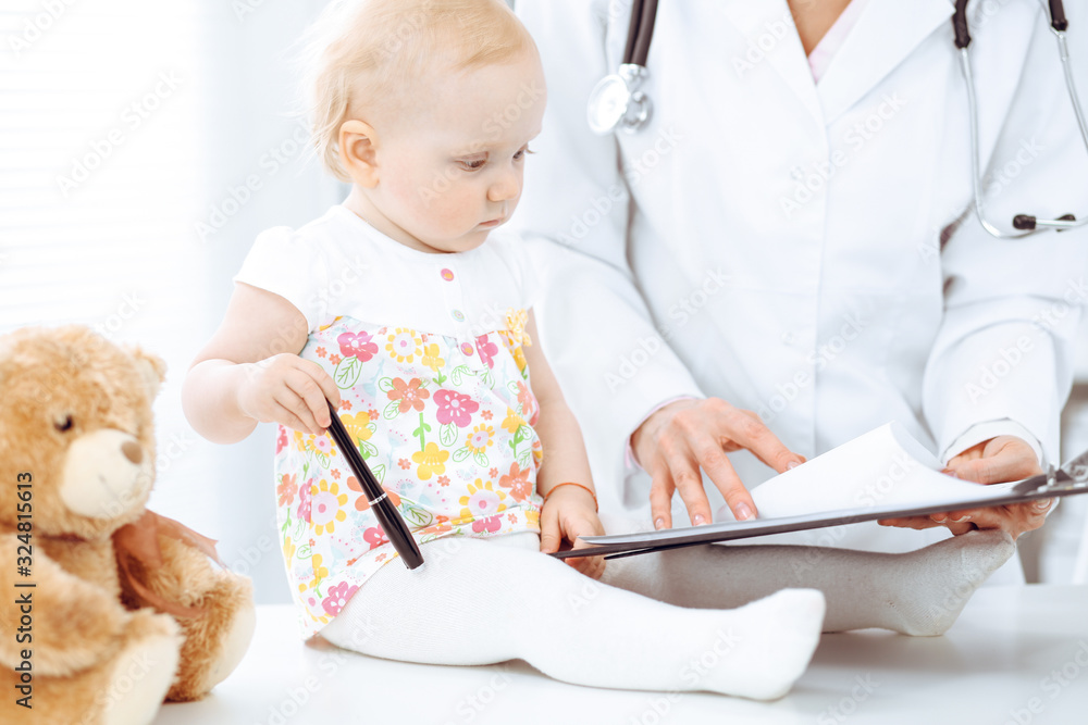 Doctor and patient toddler in hospital. Little girl dressed in dress with pink flowers is being examined by doctor with stethoscope. Medicine concept Doctor and patient toddler in hospital. Little girl dressed in dress with pink flowers is being examined by doctor with stethoscope. Medicine concept