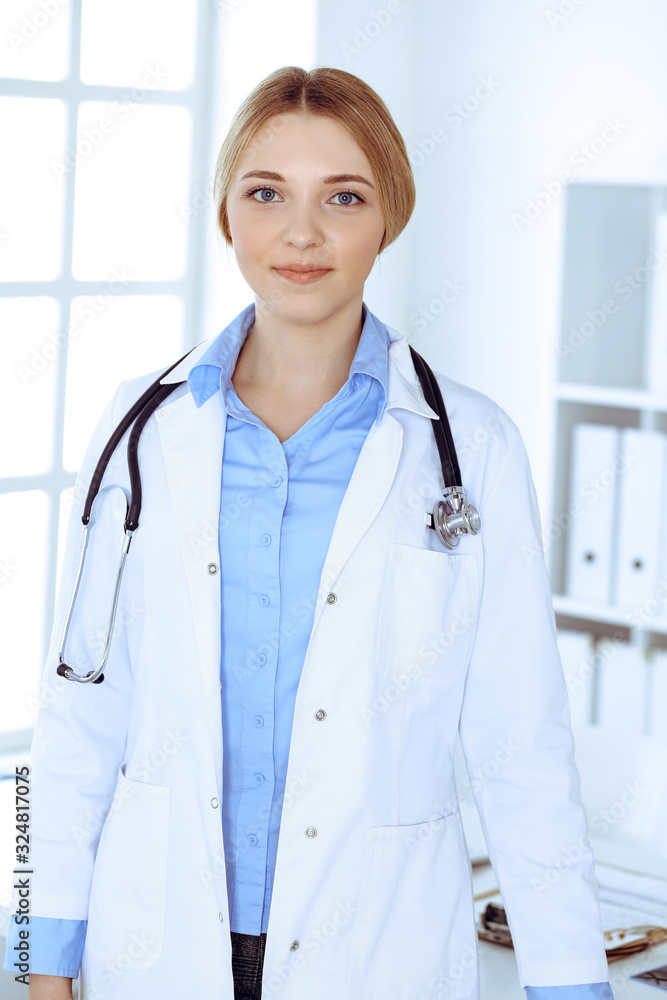 Young woman doctor at work in hospital looking at camera. Blue colored blouse of therapist looks good. Medicine and healthcare concept