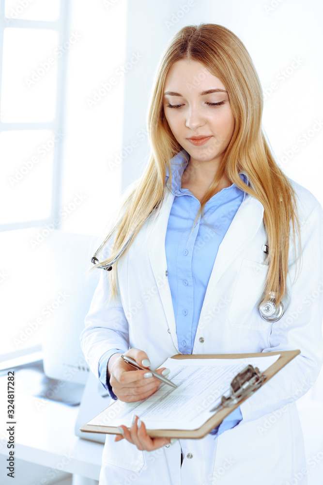 Young woman doctor at work in hospital office. Blue color blouse of therapist looks good. Medicine and healthcare concept Young woman doctor at work in hospital office. Blue color blouse of therapist looks good. Medicine and healthcare concept