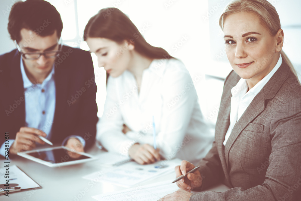 Fototapeta premium Headshot of business woman at negotiation. Group of business people discussing questions at meeting in modern office. Teamwork, partnership and business concept