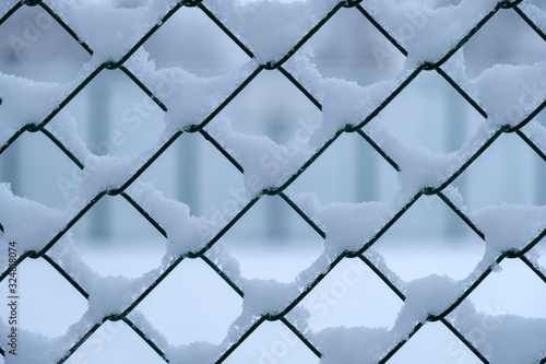 Metal mesh covered with snow. Metallic grid with snow background.